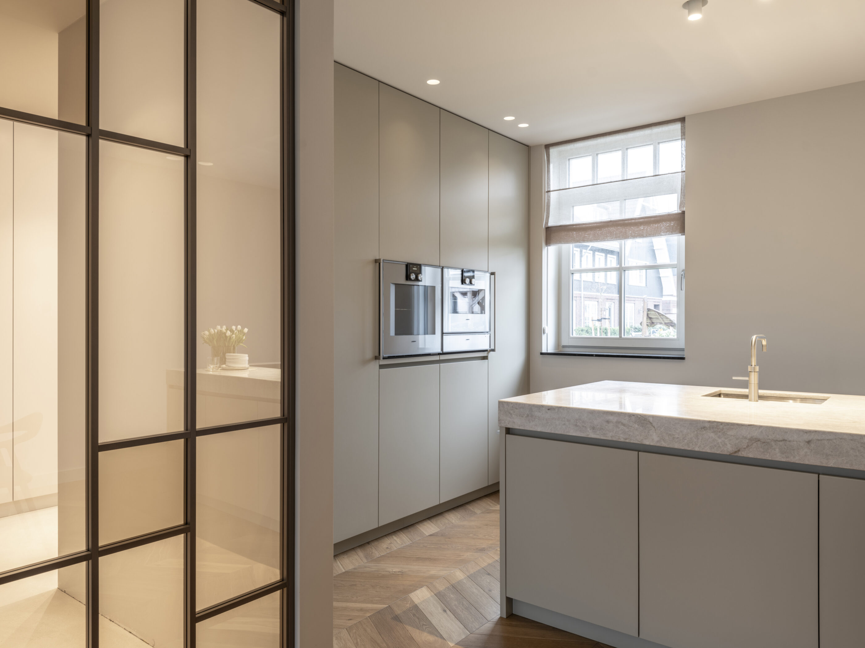 Grijze moderne keuken met kookeiland, afgewerkt met Taj Mahal natuursteen en zachte lijnen voor een luxe uitstraling.