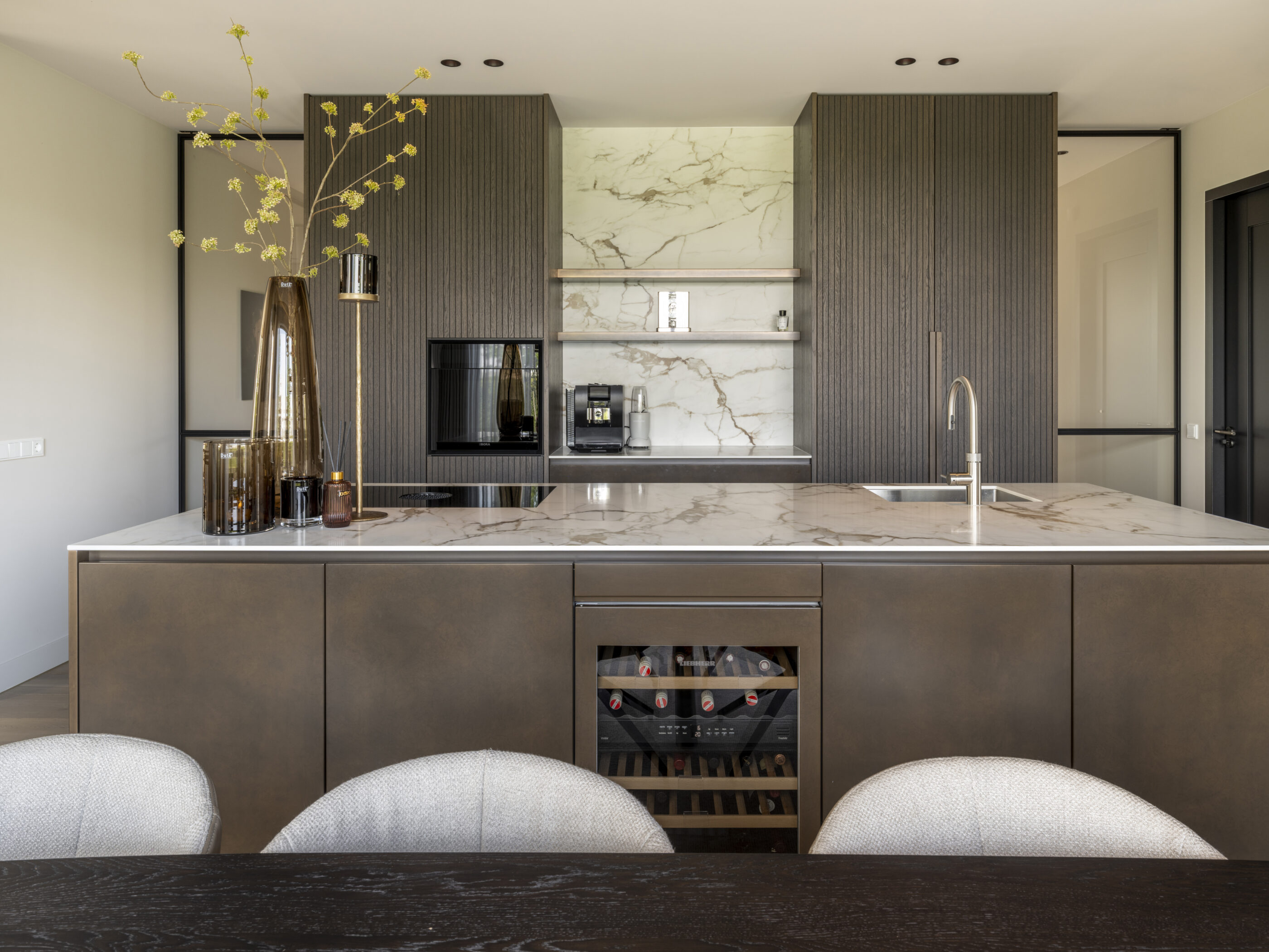 Eigentijdse luxe keuken met tabak-kleurige fronten, brons patiné accenten en een keramiek werkblad in calacatta macchia vecchia silk.