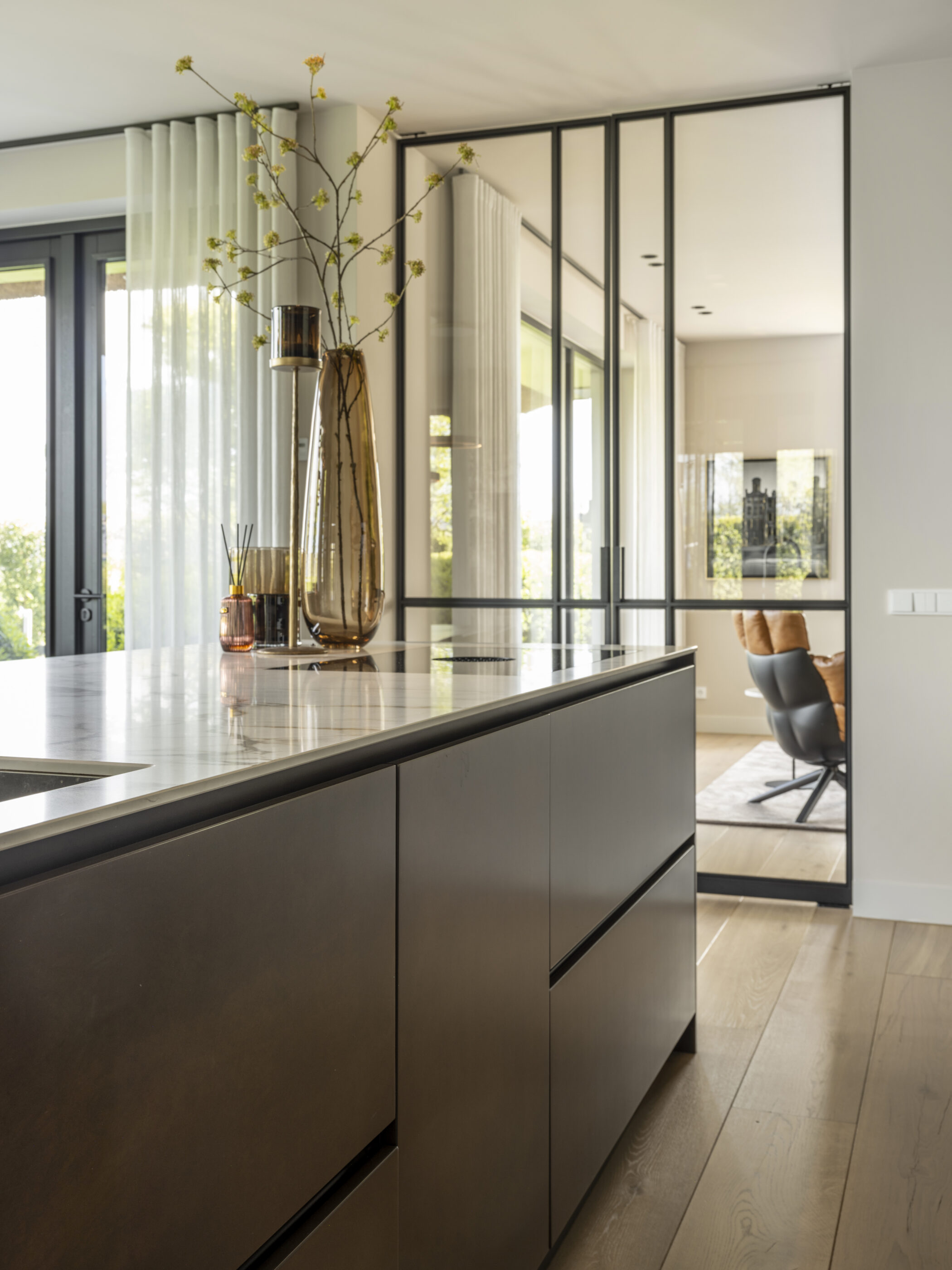 Moderne keuken met brons patiné kookeiland en stalen deuren als stijlvolle verbinding naar de woonkamer.
