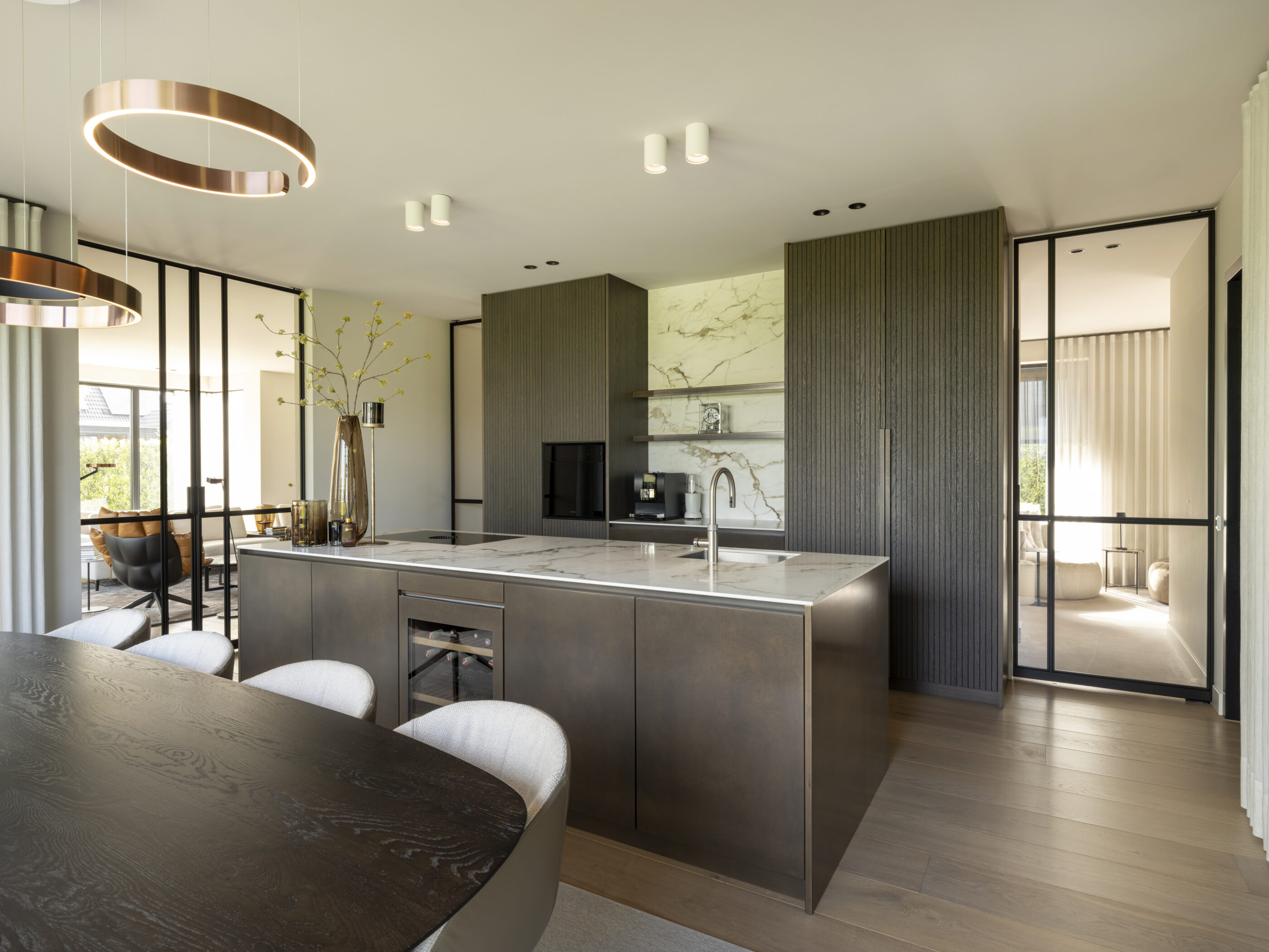 Luxe designkeuken met tabak-kleurige kastenwand, brons patiné kookeiland en keramiek werkblad in calacatta macchia vecchia silk.