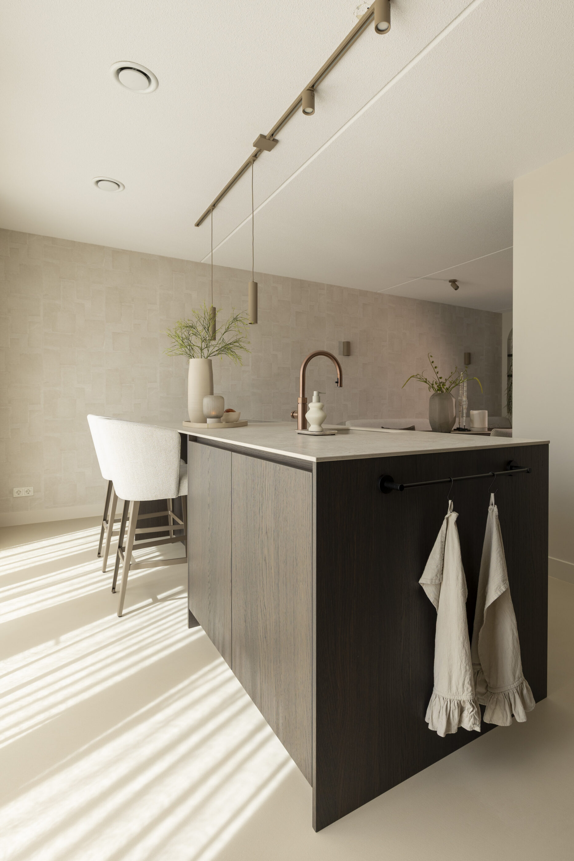 Kookeiland in donker eikenfineer met geïntegreerde spoelzone en zitgedeelte met beige barkrukken in een moderne leefkeuken.