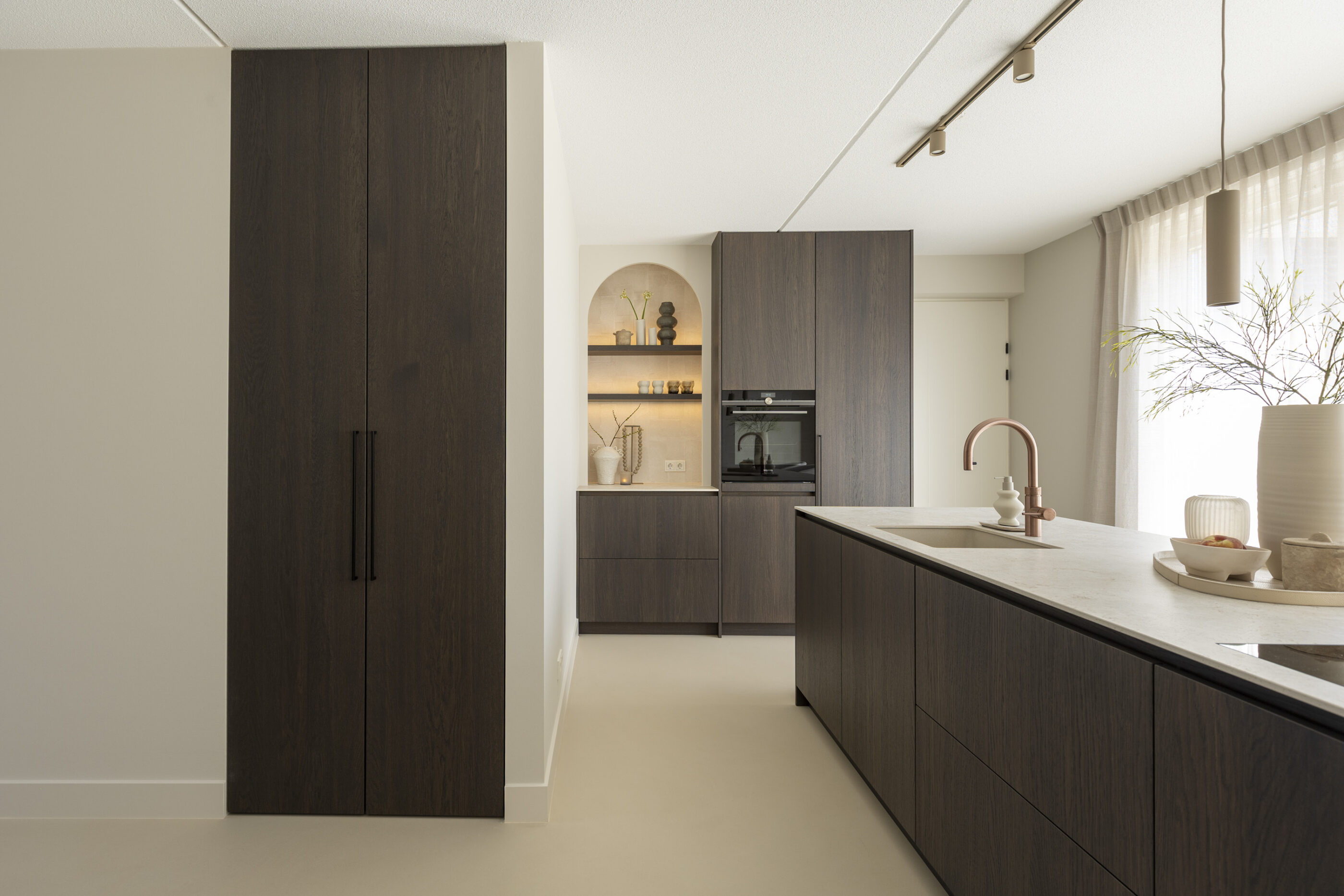 Open leefkeuken met donker eikenfineer keuken die naadloos overgaat in de woonkamer met een ruimtelijk en warm interieurontwerp.