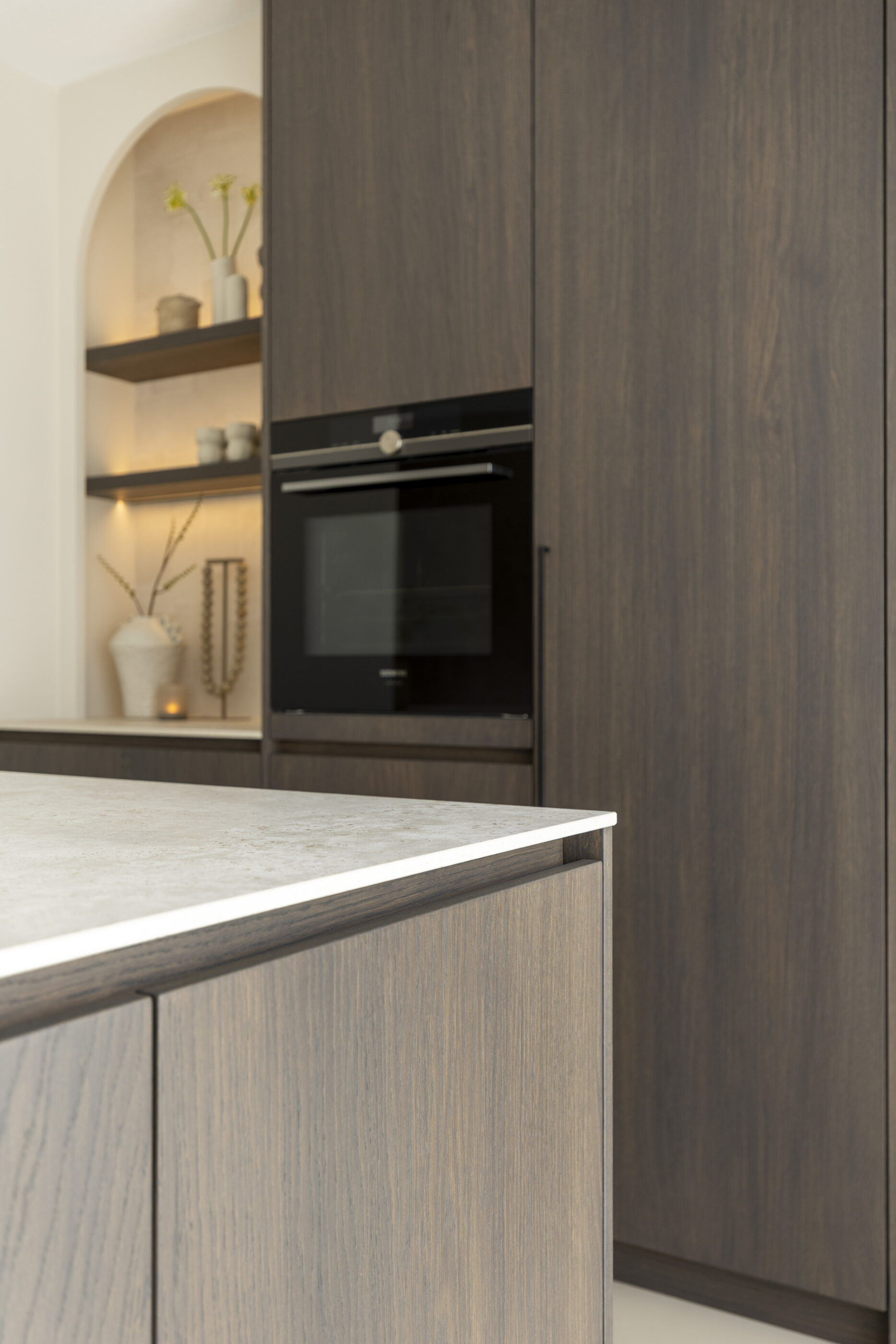 Close-up van werkblad in lichte natuursteenlook gecombineerd met donker eikenfineer keukenkasten in een luxe maatwerk keuken.