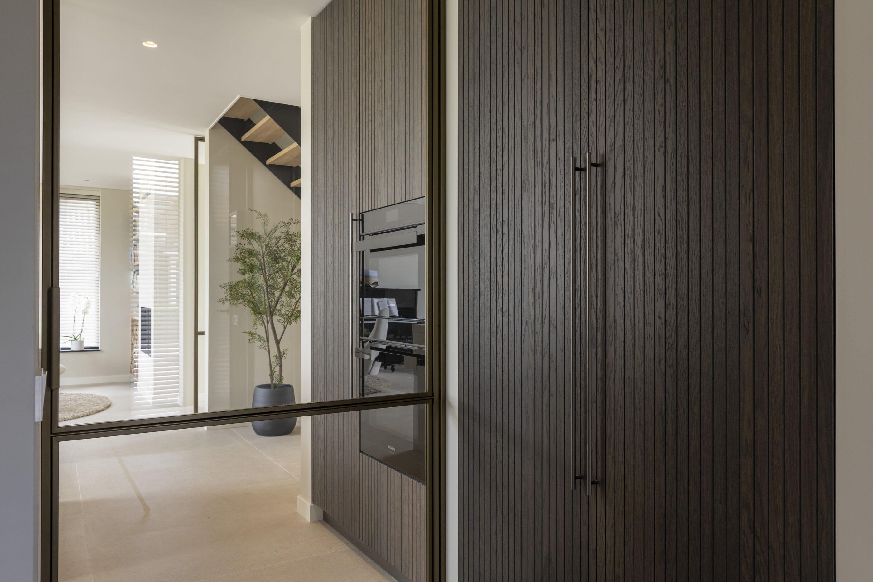 Donkere houtlook keukenwand met hoge maatwerkkasten, geïntegreerde Siemens apparatuur en een warme, luxe uitstraling.